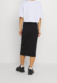 Avskuren ljusgrå t-shirt i kombination med en ribbad svart midikjol, bärs med svarta sneakers. Strukturerat tyg och enkel design.