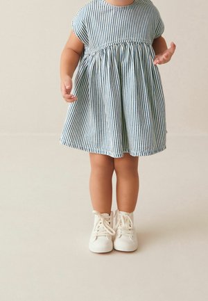 Robe rayée bleu et blanc avec une taille froncée, des manches courtes et une jupe évasée. Associée à des chaussures blanches à lacets.