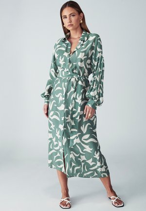 Ilgas, su mygtukais užsegamas suknelė šviesiai žalios spalvos audinio su balta gėlių raštu. Yra diržo juosmuo ir pūkuotos rankovės.