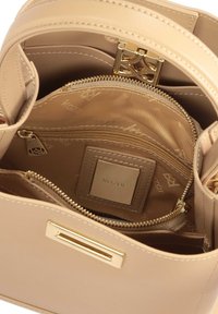 Sac à main structuré beige avec quincaillerie dorée, comprenant un compartiment zippé et un motif intérieur en relief affichant le logo de la marque.