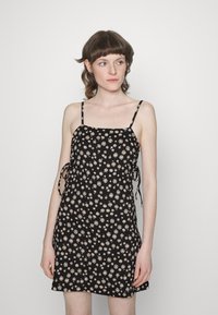 Vestido preto com alças ajustáveis, coberto com pequenos padrões florais em bege. Tecido suave com um ajuste solto e laços laterais.