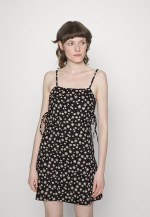 Vestido preto com alças ajustáveis, coberto com pequenos padrões florais em bege. Tecido suave com um ajuste solto e laços laterais.