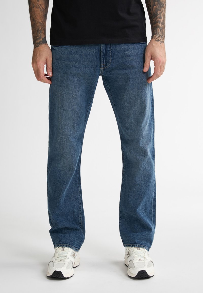 Blauwe spijkerbroek met een rechte pasvorm, voorzien van een klassieke vijf-pocketsontwerp en lichte vervaging, gecombineerd met witte sneakers.
