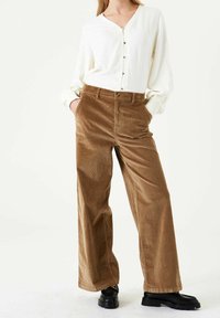 Cream button-up shirt with long sleeves paired with high-waisted, wide-leg corduroy pants in brown, complemented by black chunky shoes.
