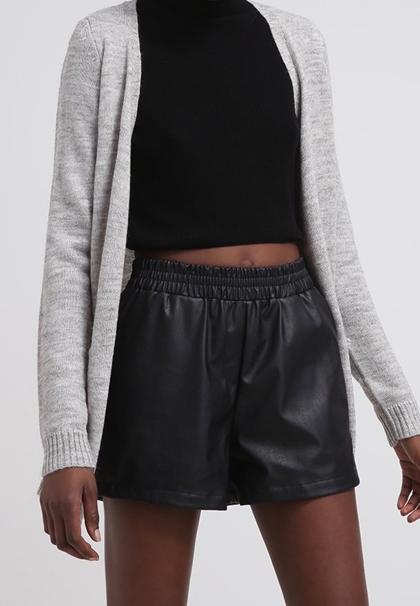 Grå stickad cardigan över en svart ribbad polokrage, parat med svarta shorts i imitationläder med elastisk midja.