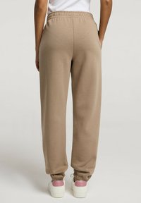 Beżowe dresy z elastycznym pasem, zwężanymi mankietami i gładką fakturą, w połączeniu z białymi sneakersami z różowymi akcentami.