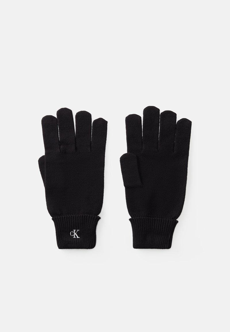 Luvas de malha pretas com pontas dos dedos expostas, punhos canelados e um pequeno logo bordado no pulso. Textura suave e design ajustado.