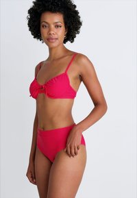 Rdeč bikini set, ki vsebuje zavezani vrh bralete z tankimi naramnicami in visokim pasom. Gladka tkanina z enotno barvo.