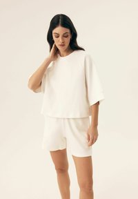 Weißes Loungewear-Set bestehend aus einem locker sitzenden, kurzärmligen Oberteil und passenden Shorts, aus weichem Stoff mit glatter Textur.