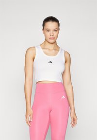 Top cropped branco com logo preto, combinado com leggings cor-de-rosa com logo branco. Tecido suave, design ajustado e costuras mínimas.