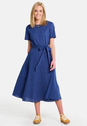 Robe en lin bleu avec une coupe décontractée, des manches courtes et une ceinture nouée à la taille. Associée à des baskets jaunes pour un look décontracté.