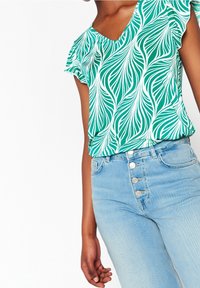 Bluzka z krótkim rękawem w zielony wzór liści, z dekoltem w serek, wykonana z lekkiego materiału, zestawiona z jasnoniebieskimi spodniami o wysokim stanie, posiadającymi pięć guzików.