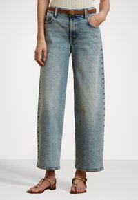 Gaiši zili plaša piegriezuma džinsi no denima, ar augstu vidukli un saplaisājušu apakšmalu. Saskaņoti ar brūnu jostu un smilšu krāsas sandalēm.