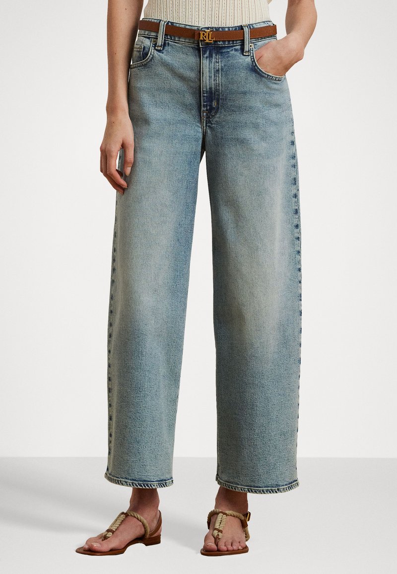 Gaiši zili plaša piegriezuma džinsi no denima, ar augstu vidukli un saplaisājušu apakšmalu. Saskaņoti ar brūnu jostu un smilšu krāsas sandalēm.