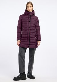 Paarse gewatteerde jas met een capuchon, voorzien van een rits aan de voorkant en knoopsluiting, zwarte accenten en een gestikte textuur. Gecombineerd met grijze jeans en zwarte laarzen.