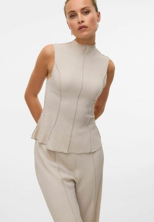 Haut sans manches beige avec un col montant, en tissu texturé et avec des coutures, assorti à un pantalon texturé de teinte similaire.