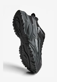 Čierna športová obuv s texturovanou gumovou podrážkou, zosilnenou špičkou, sieťovými panelmi a ťahacím pásikom vzadu. Obsahuje zakrivené línie dizajnu.