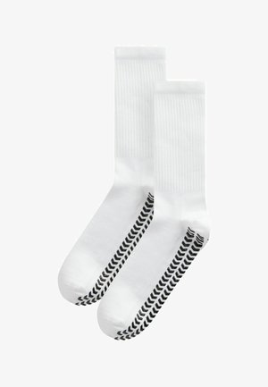Chaussettes blanches avec une texture côtelée et un motif en chevron noir sur les côtés. Le design est à hauteur de cheville avec une zone de orteil renforcée.