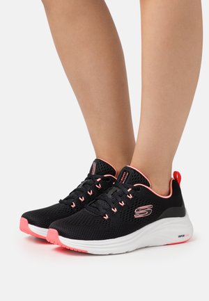 Schwarze Sportsneaker aus Mesh-Gewebe, mit pinken Akzenten, Schnürdesign und gepolsterter weißer Sohle. Mit Logo an der Seite.