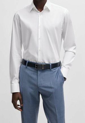Camicia bianca a maniche lunghe con colletto classico, abbinata a pantaloni grigi chiari con texture e una cintura nera con fibbia in argento.