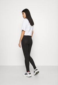 Leggings noirs avec une taille haute, texture lisse. Associés à un t-shirt blanc à manches courtes et des chaussures de sport noir et blanc.