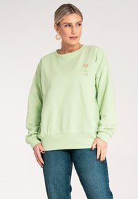 Miętowy sweter z okrągłym dekoltem, ribbowymi mankietami i dołem. Posiada haftowany kieliszek wina i napis "rosé" na klatce piersiowej.