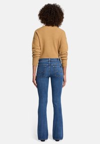 Blauwe flared denim jeans met hoge taille, voorzien van twee achterzakken met gebogen stiksels, gecombineerd met een beige, ontspannen-fit trui.