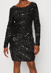 Czarna sukienka z cekinami, z długimi rękawami, dopasowaną sylwetką, okrągłym dekoltem i fakturowaną powierzchnią utworzoną przez gęste, połyskujące cekiny.