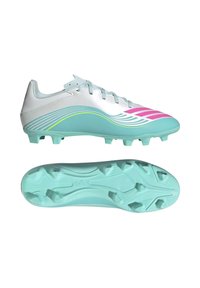 Chaussure de football blanche et turquoise avec des accents rose et jaune, présentée de côté et en vue de la semelle avec des crampons moulés pour terrain ferme.