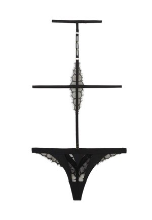 Lingerie string en dentelle noire avec bretelles réglables et détails en maille à bord festonné, étalée à plat sur un fond blanc.