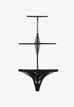 Lingerie string en dentelle noire avec bretelles réglables et détails en maille à bord festonné, étalée à plat sur un fond blanc.