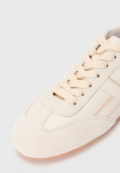 Beżowe zamszowe i skórzane sneakersy z dopasowanymi beżowymi sznurówkami i detalami szytymi, pokazane z widoku z góry w zbliżeniu.