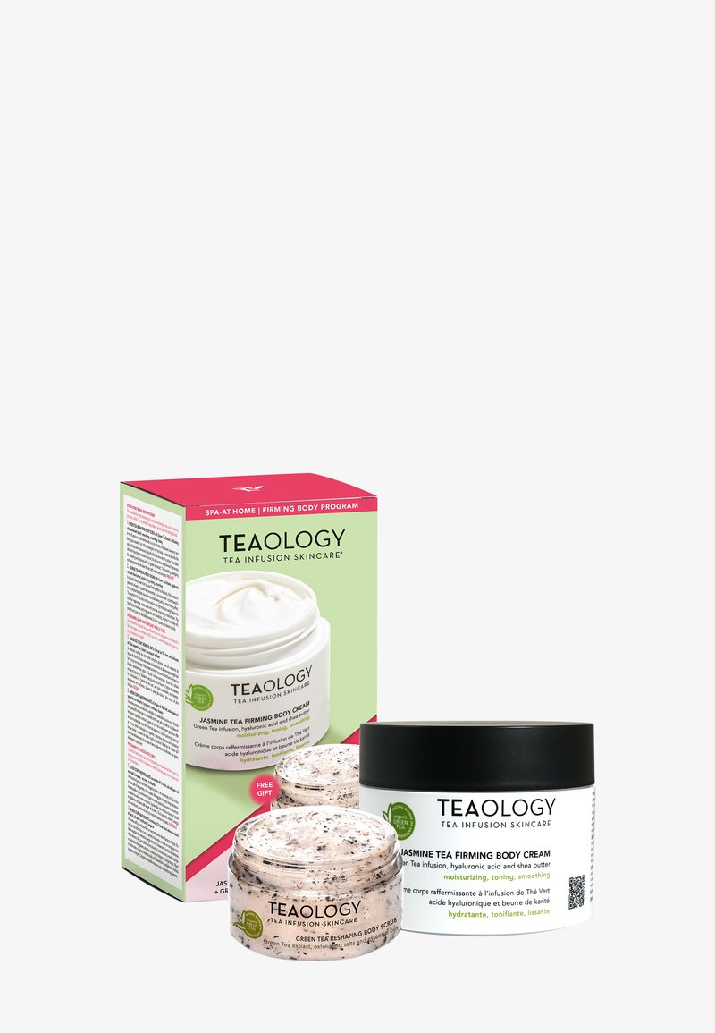 Le set de soins Teaology comprend un pot blanc avec de la crème et un pot de gommage à la texture mouchetée, tous deux dans un emballage noir et blanc. La boîte présente des accents vifs de rose et de vert.