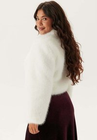 Maglione bianco fluffy cropped con maniche lunghe, abbinato a una gonna viola scura, caratterizzata da una texture morbida e un design minimalista.