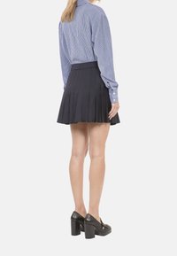 Blau-weiße gestreifte Langarmbluse, schwarzer Faltenrock und schwarze Absatzschuhe. Das Outfit hat ein lässiges Design aus strukturiertem Material.