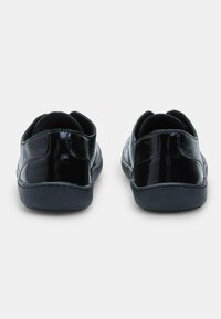Juodos, blizgios odinės slip-on tipo batų pora, matoma iš nugaros, ant neutralios baltos paviršiaus.