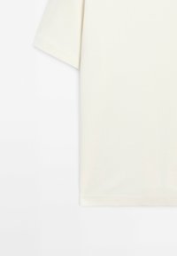 Off-white kortärmad T-shirt visad från midjan till ärmslut mot en vit bakgrund, vilket framhäver tygtextur och sömmar.