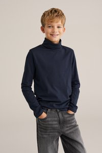 Marinblå polo-tröja i mjuk bomull, tillsammans med urtvättade svarta jeans. Långa ärmar och en avslappnad passform framhäver en avslappnad stil.