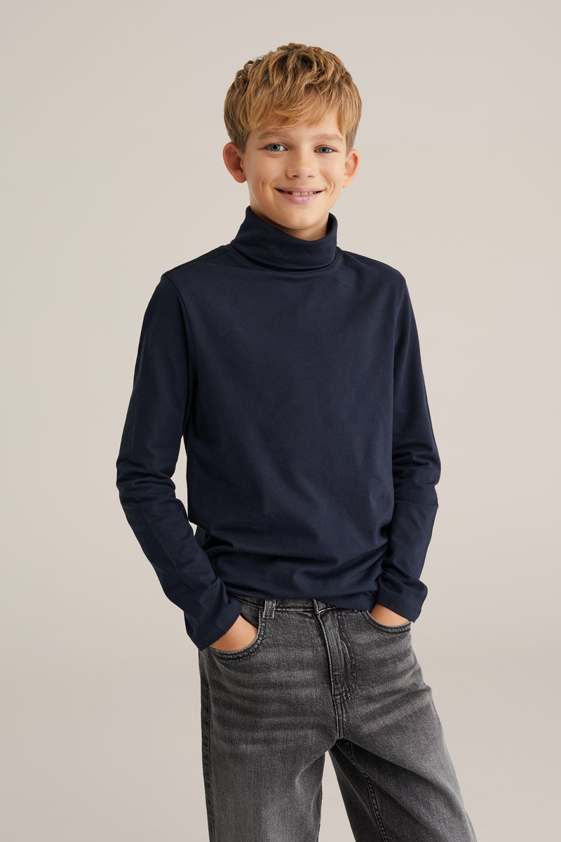 Marinblå polo-tröja i mjuk bomull, tillsammans med urtvättade svarta jeans. Långa ärmar och en avslappnad passform framhäver en avslappnad stil.