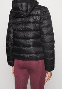 Svart puffjacka med huva, med en kviltad design och blank yta. Kombineras med maroon ormtryckta leggings.