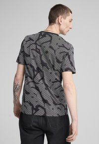 Kortærmet sort t-shirt med et hvidt tekstmønster, rund halsudskæring og afslappet pasform, lavet af et let og åndbart stof.