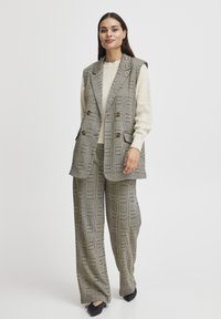 Gilet à carreaux et pantalon large dans des tons gris et crème, doté de boutons croisés et d'un pull en maille texturée en dessous.