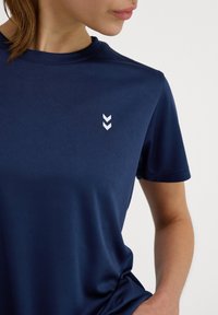 Granatowa koszulka T-shirt z krótkim rękawem, wykonana z gładkiego materiału, z małym białym logo w kształcie chevroń na klatce piersiowej i klasycznym okrągłym dekoltem.