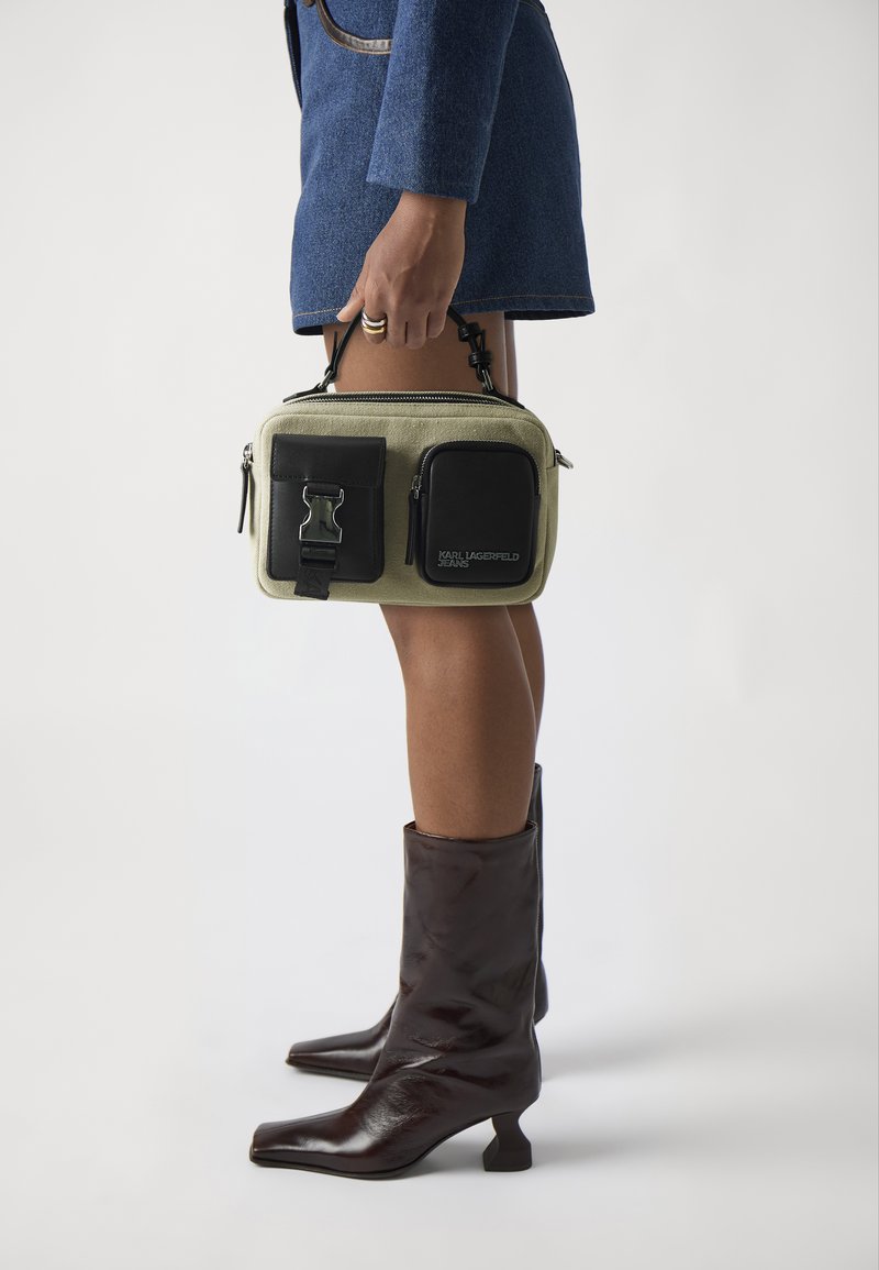 Olive green rectangular bag with black accents, two zippers, and a front pocket. Features a short handle and a clip closure.