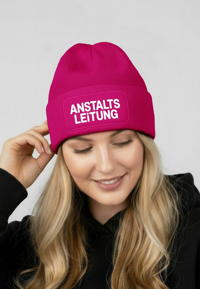 Fuchsia knit beanie with a fold-over design and white text reading "ANSTALTSLEITUNG," featuring a smooth texture and snug fit.