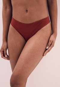 Röd bikiniunderdel med högskuren, minimalistisk design. Slät textur och elastiskt band runt midjan, utan synlig hårdvara eller mönster.
