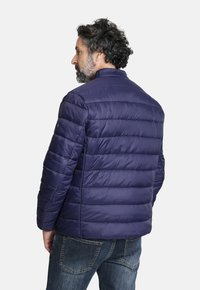 Chaqueta acolchada azul marino con diseño de costura horizontal y cuello alto, hecha de material suave y ligero; combinada con jeans de mezclilla.