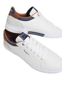 White leather sneakers with brown and navy accents, textured sides, round toe, and a lace-up front. Features logo detail and rubber sole.