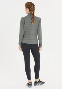 Grå sportsjakke med quiltet ryg, lange ærmer og høj krave, parret med sorte leggings og sorte træningssko.