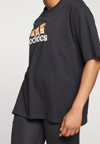 Black cotton t-shirt with a loose fit, featuring a multicolored graphic design of "adidas" and floral accents on the front.